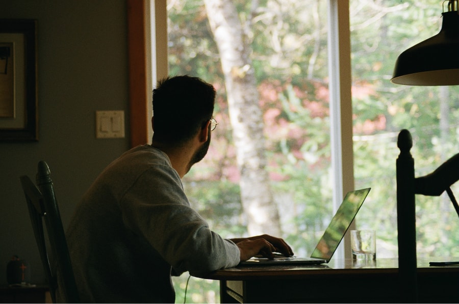 Jovem sentado numa secretária ao computador e a olhar para a janela numa alusão a um período de reflexão após a leitura de uma das nossas recomendações de livros para marketing digital