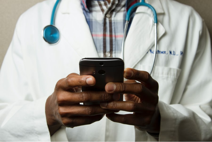 Médico de bata e estetoscópio ao pescoço consulta o seu telemóvel, como exemplo de comunicação e marketing em clínicas e centros médicos